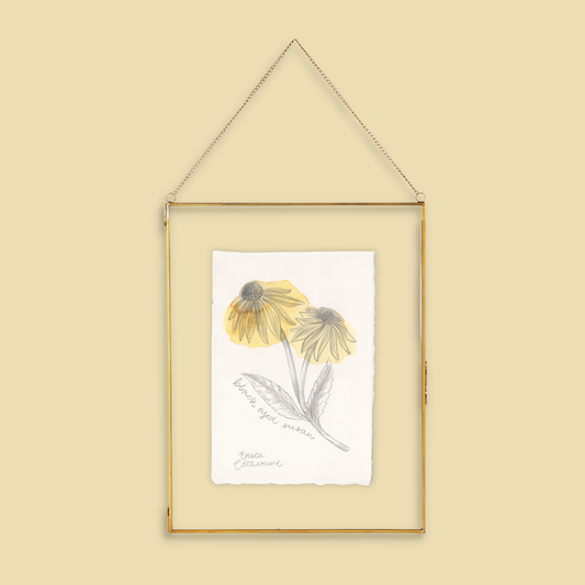 A framed botanical art print featuring two yellow coneflower "Black Eyed Susan" with gray-green leaves, hanging in a thin gold frame against a solid beige background.