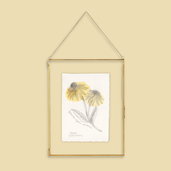 A framed botanical art print featuring two yellow coneflower "Black Eyed Susan" with gray-green leaves, hanging in a thin gold frame against a solid beige background.