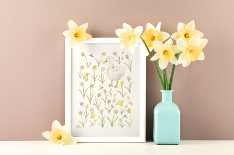 Framed artwork with a duck and her babies with flowers next to a vase with yellow flowers on a beige background