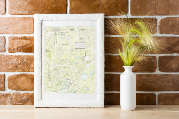 Framed map on a wooden surface with a vase of dried plants against a brick wall.