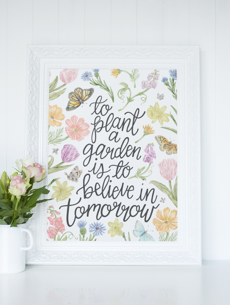 Framed floral print with quote "To Plant a Garden is to belive in tomorrow" on a white wall.