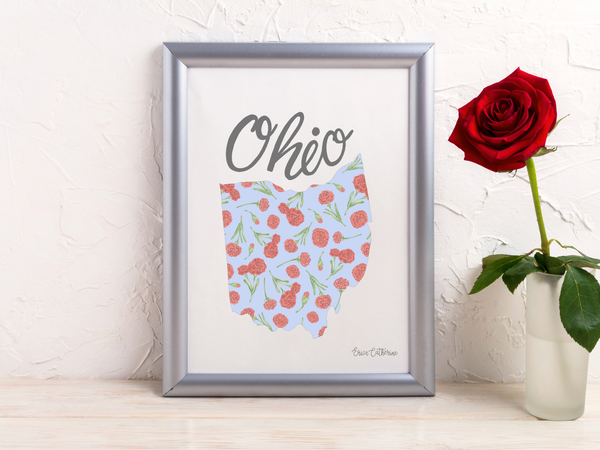 Framed map of Ohio with floral design on a white surface next to a red rose.